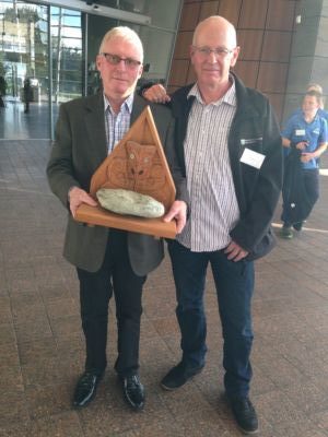 Two men hold a wooden award