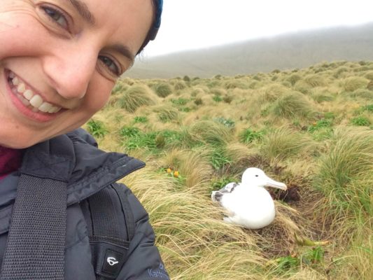 A selfie of Shona with an albatross on a nest in the background