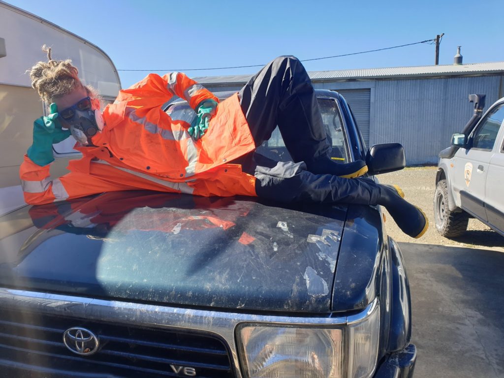 A person in full PPE lies on a car