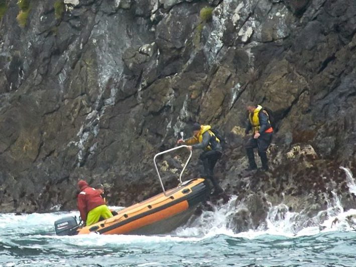 A dingy is boarded from a rocky cliff line into the ocean