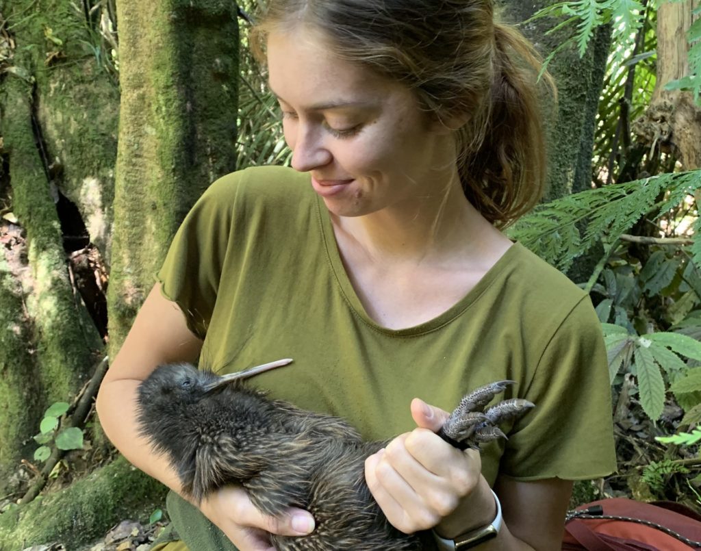 Māia holding a kiwi in the forest.