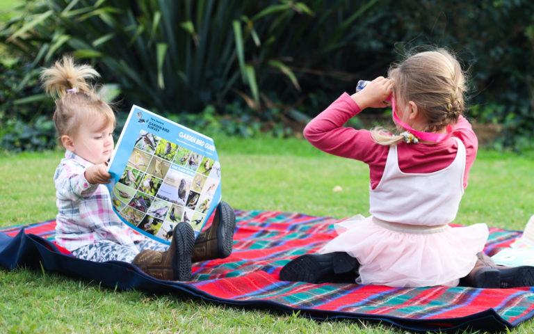 Two children sitting on a picnic mat looking for birds.