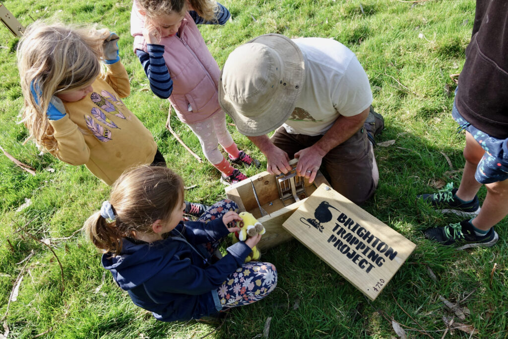 A man opening a wooden trap, showing children the inside.