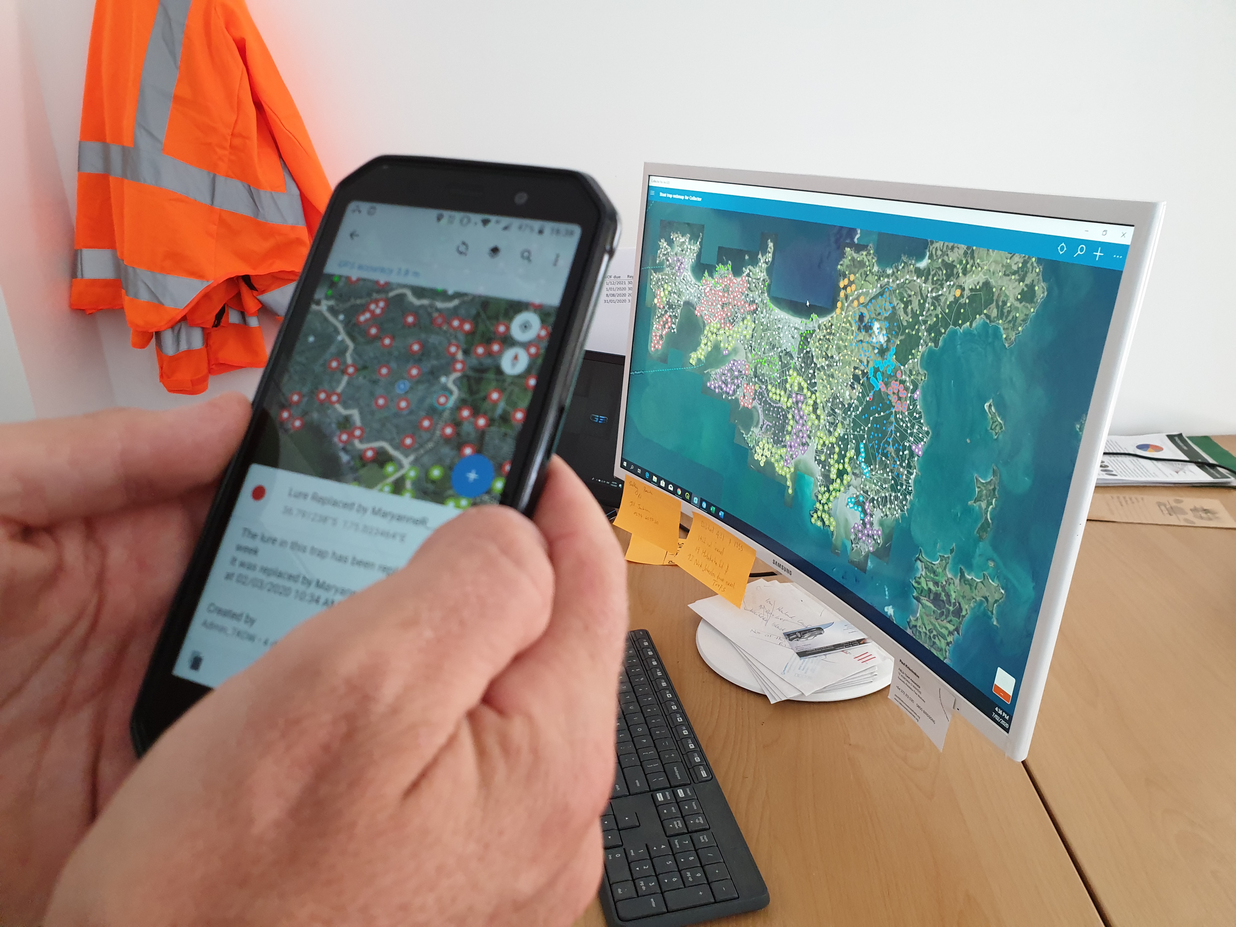 A computer screen in the background, mobile phone in foreground showing map of Waiheke Island and trap lines.