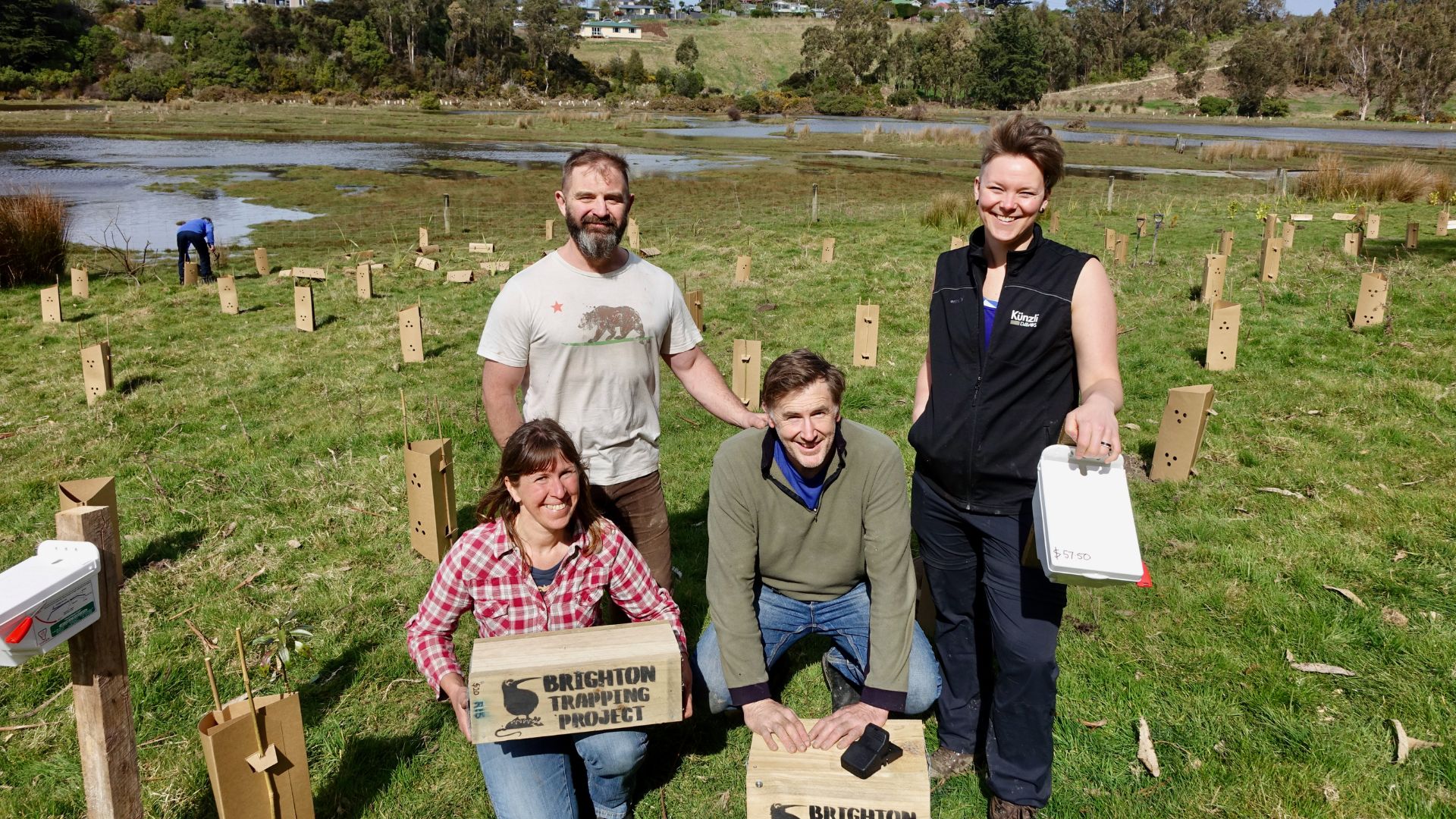 People in a field smiling next to freshly planted natives and holding trapping boxes.