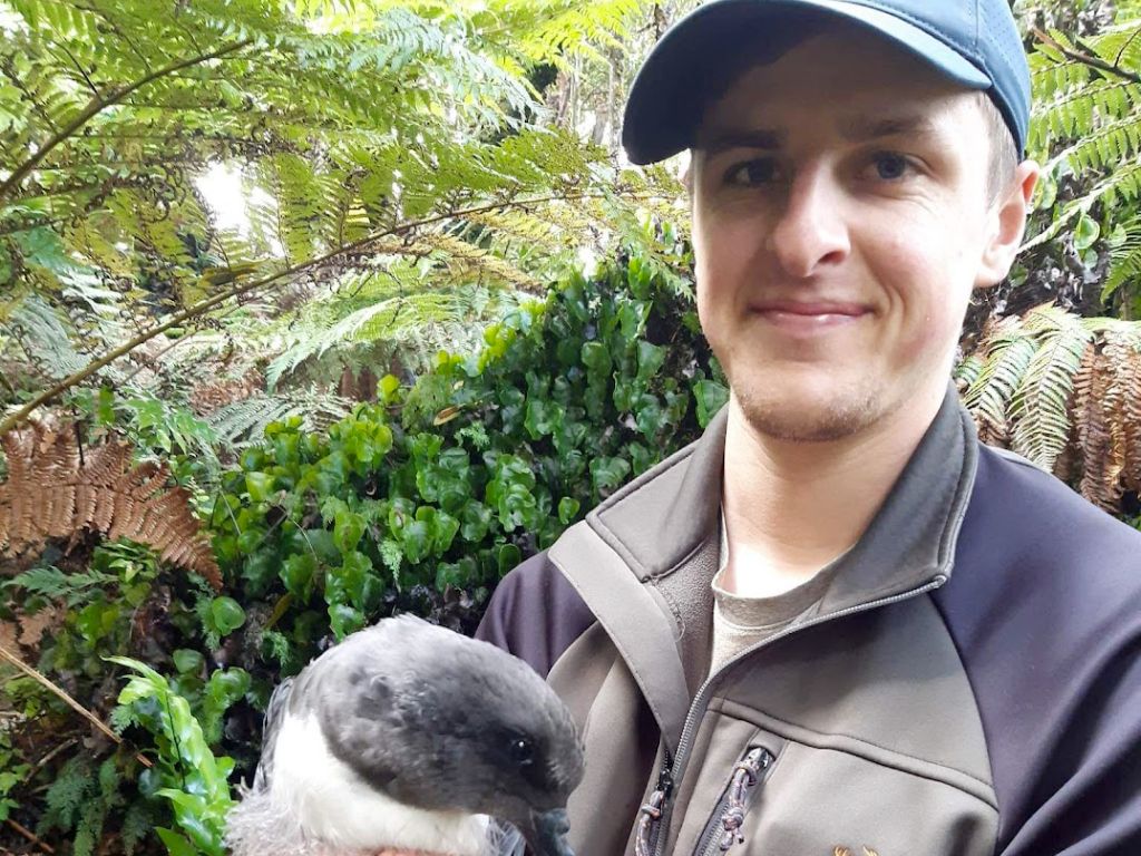 Cam, wearing a cap, looking at the camera and holding a tāiko chick