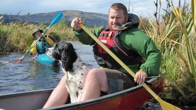 Man in a canoe with a dog, kayak in backgroun