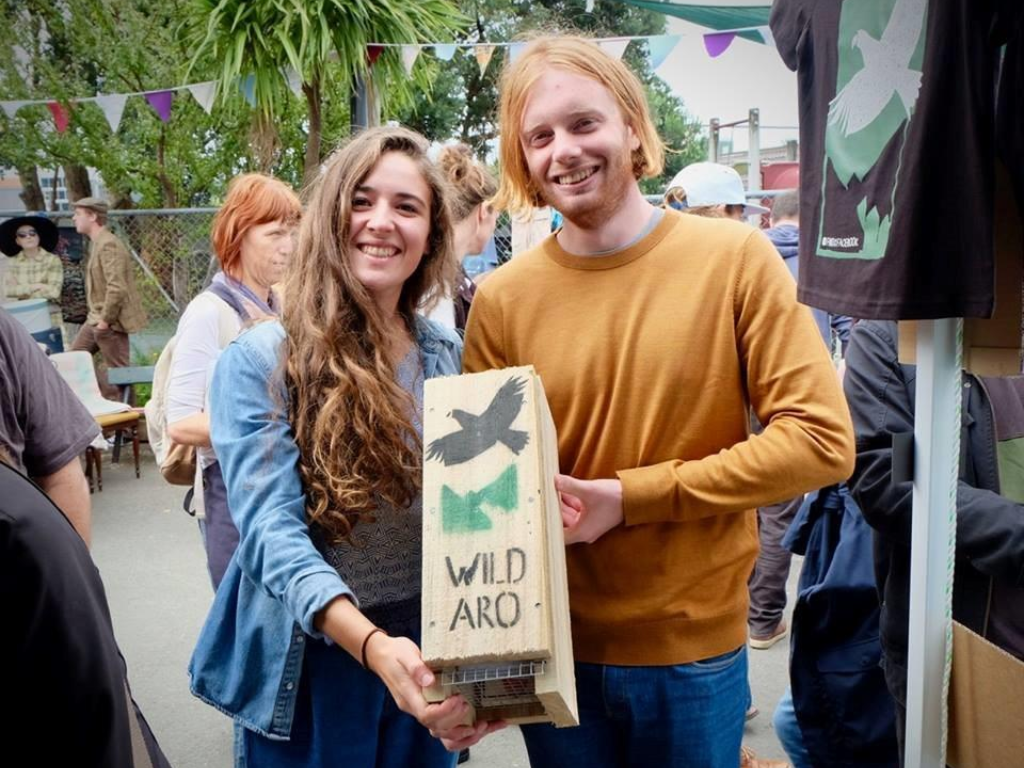 Two people stand smiling in a market holding a trap box