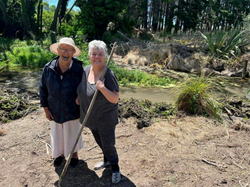 Two women standing by a river after weeding and planting along its edge