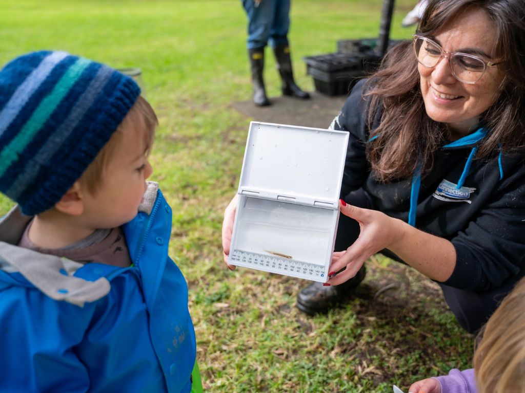 A child looking at an adult. The adult is holding a measuring device with a fish inside it.