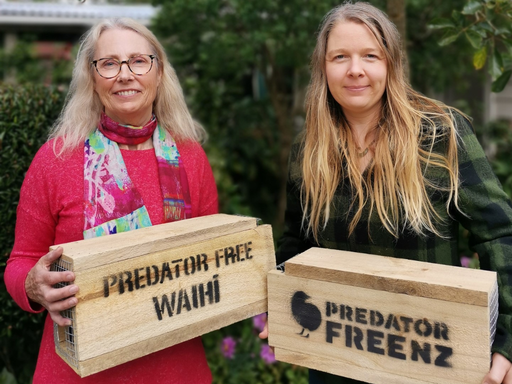 Two women stand smiling with a trap box.