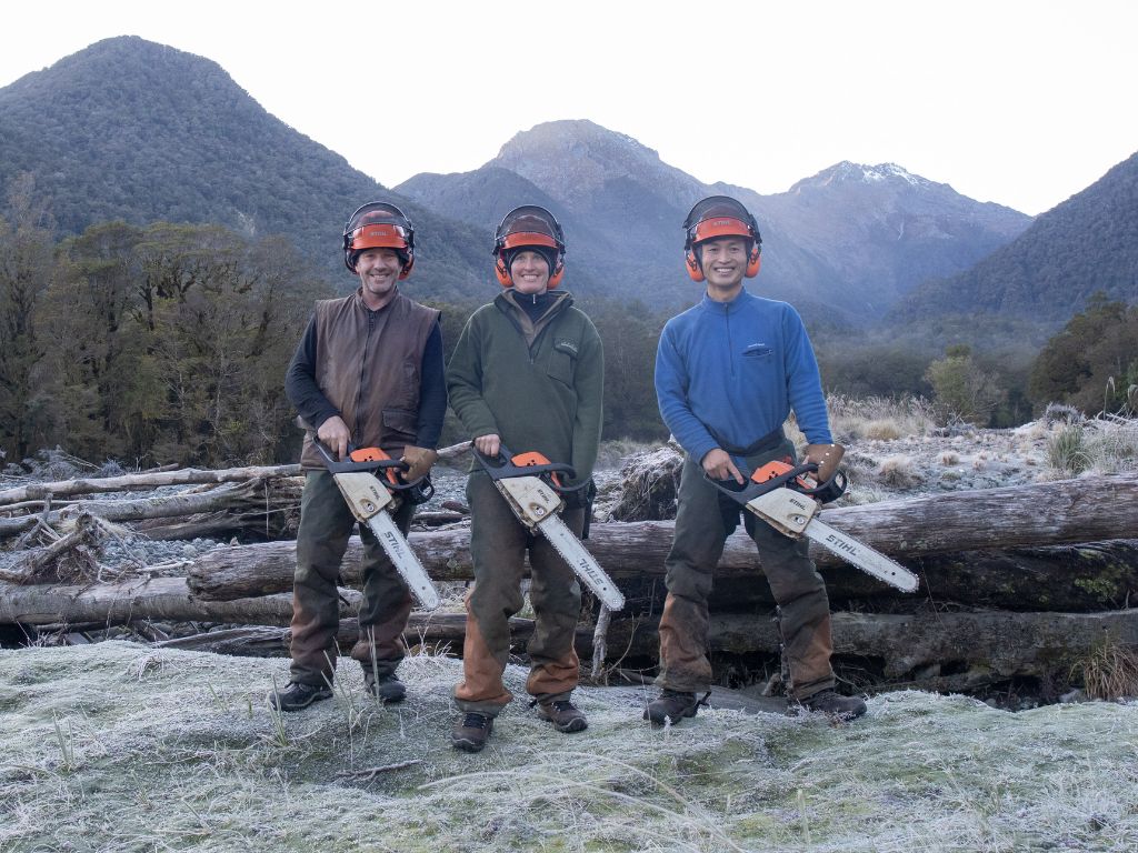 Three men with chainsaws and protective gear standing in a Fiordland valley.