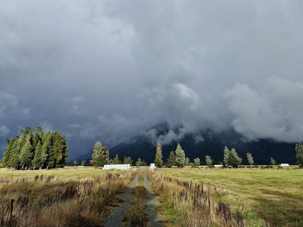 A mountain mostly hidden by clouds with farmland in the foreground.