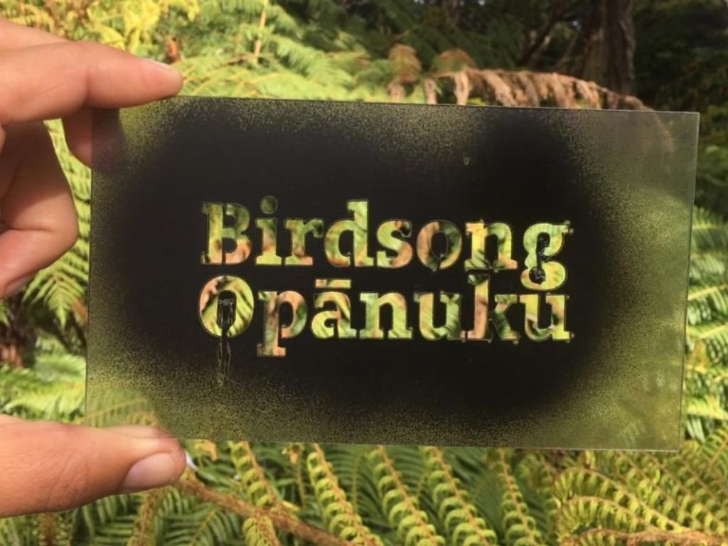 Birdsong Opanuku stencil held up against a green fern background.