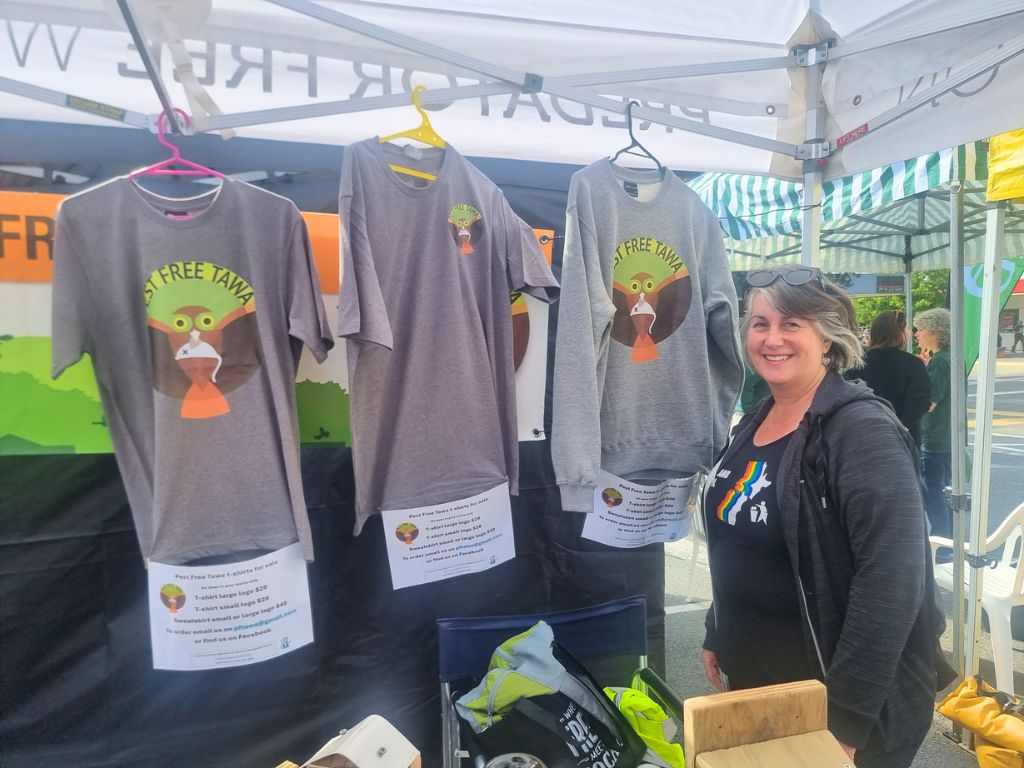 A person standing at a community stall selling Pest Free Tawa shirts.