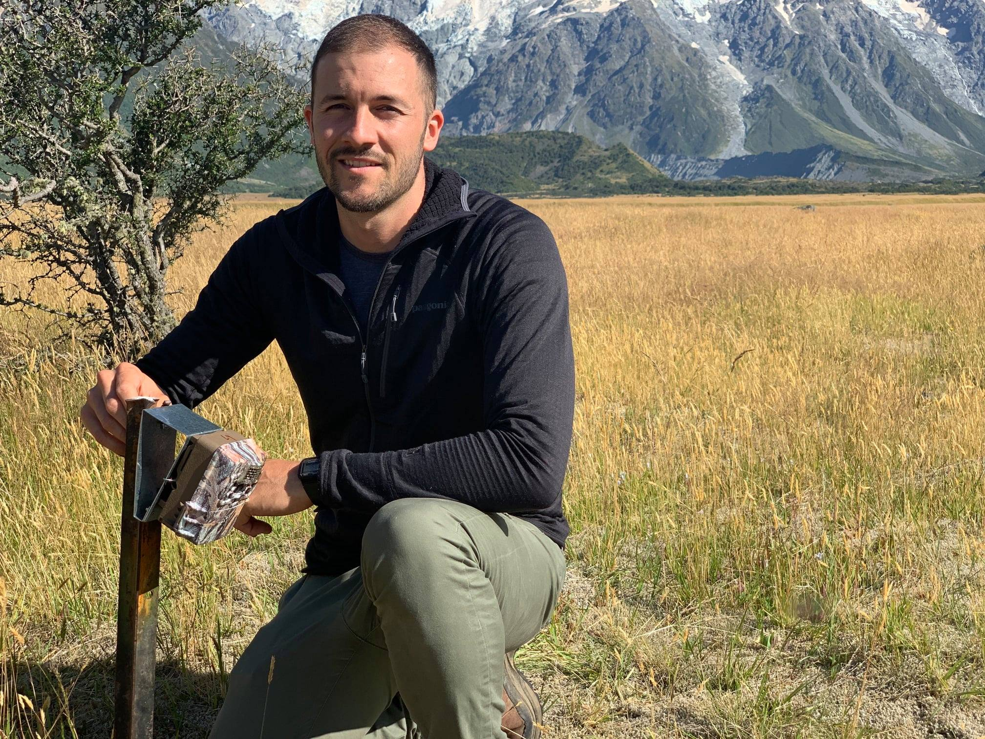 ZIP predator ecologist Nick Foster kneeling with a trail camera.