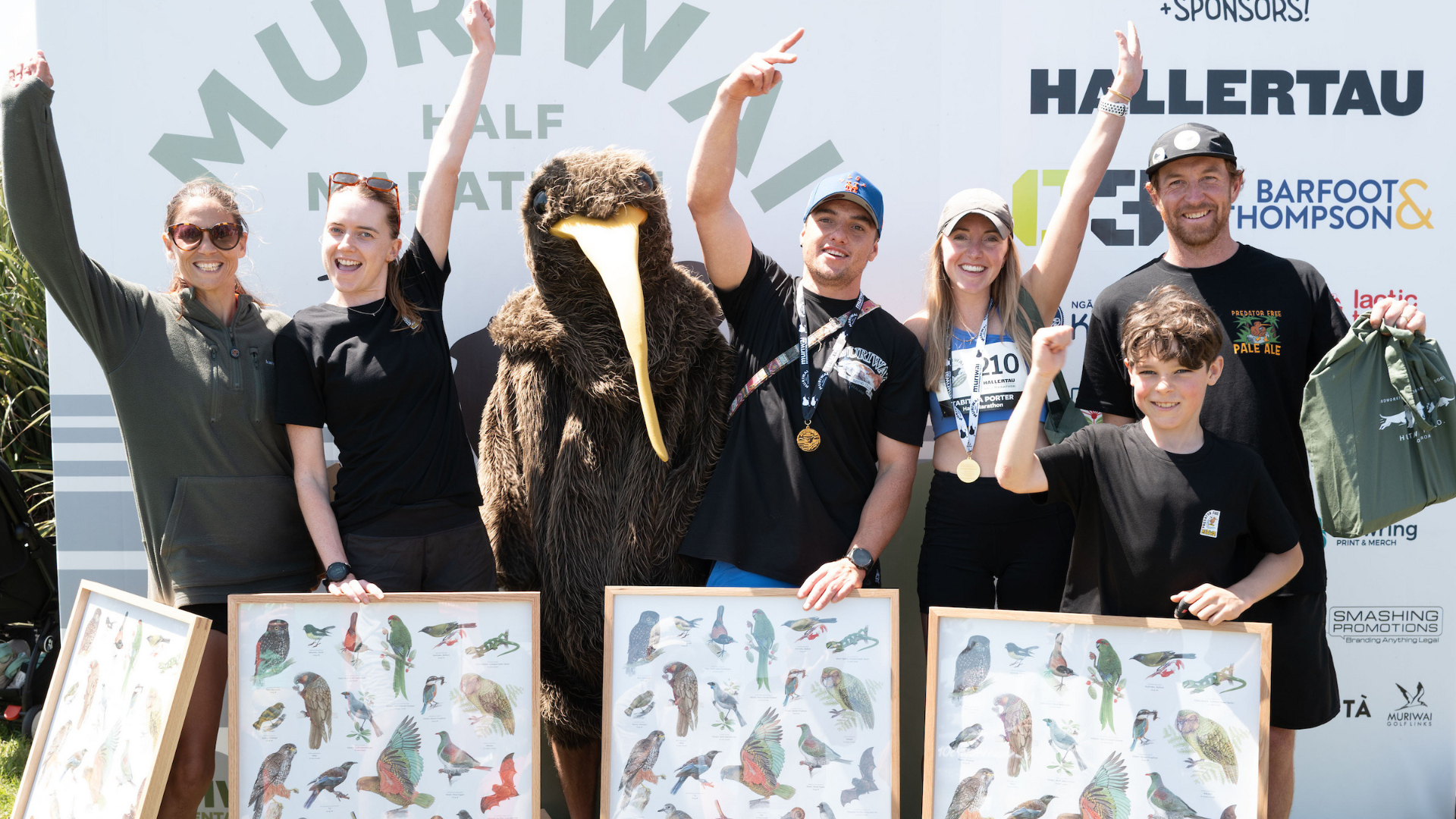 Runnings wearing medals and holding posters with NZ wildlife on them.