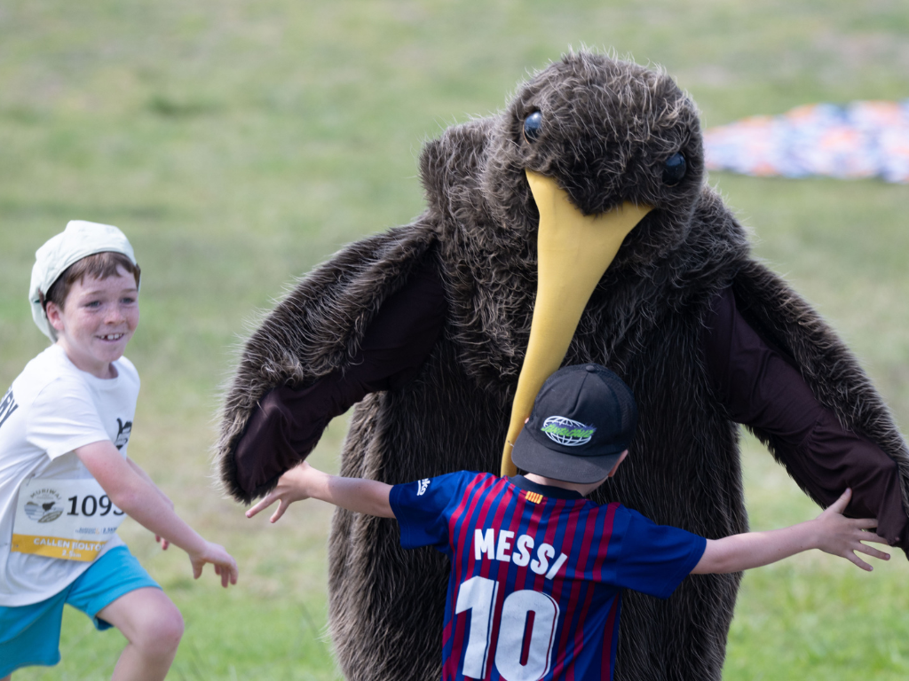 A child giving a kiwi mascot a hug