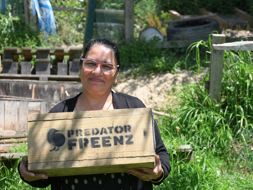 A woman holding a trap box with the predator free NZ logo
